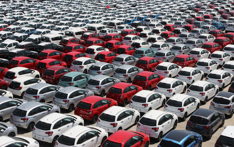 Overhead shot of neatly parked colorful cars in a large outdoor lot under sunlight.